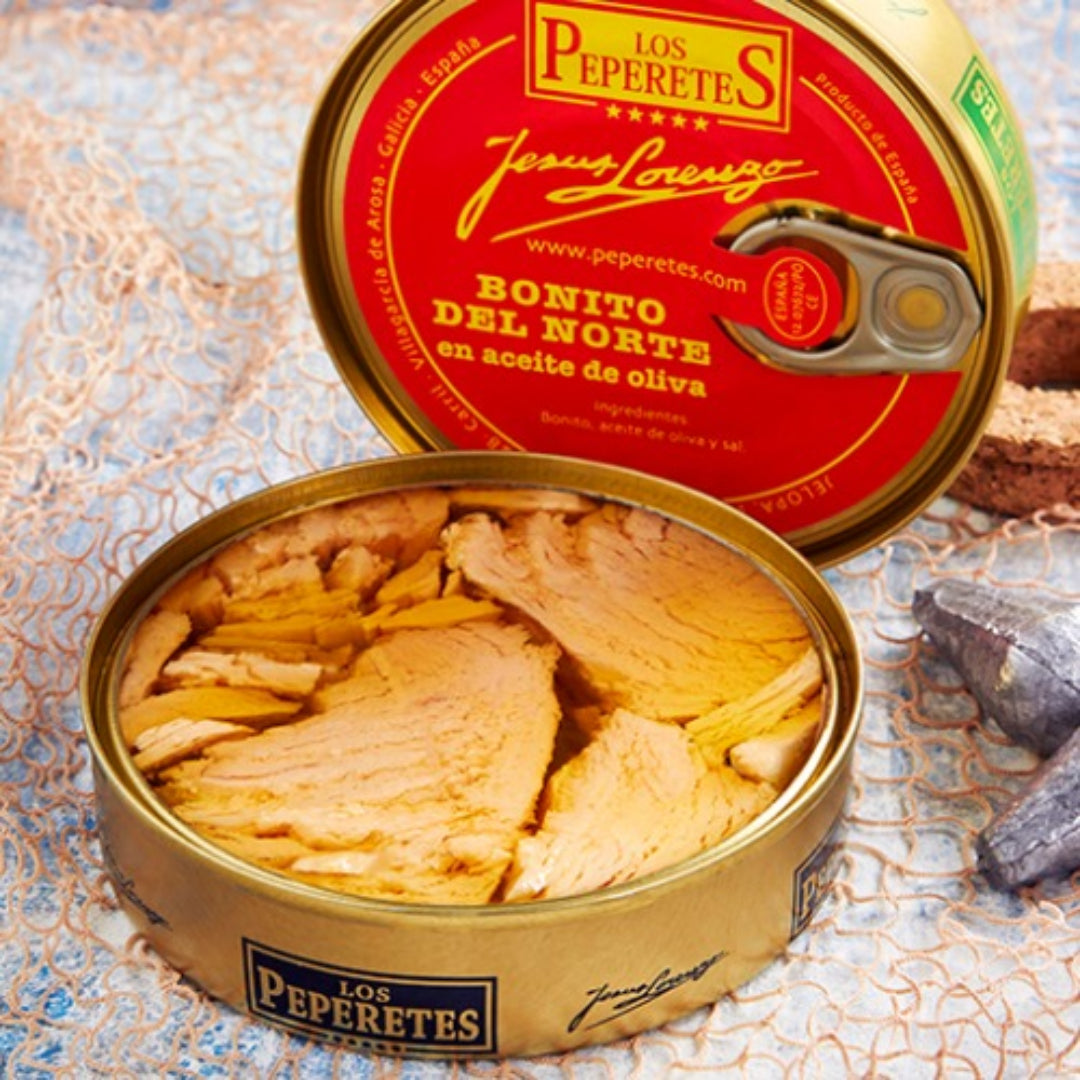 A tin can of Los Peperetes Bonito del Norte white tuna in olive oil, with the tuna visible inside the open can, placed on a textured surface.