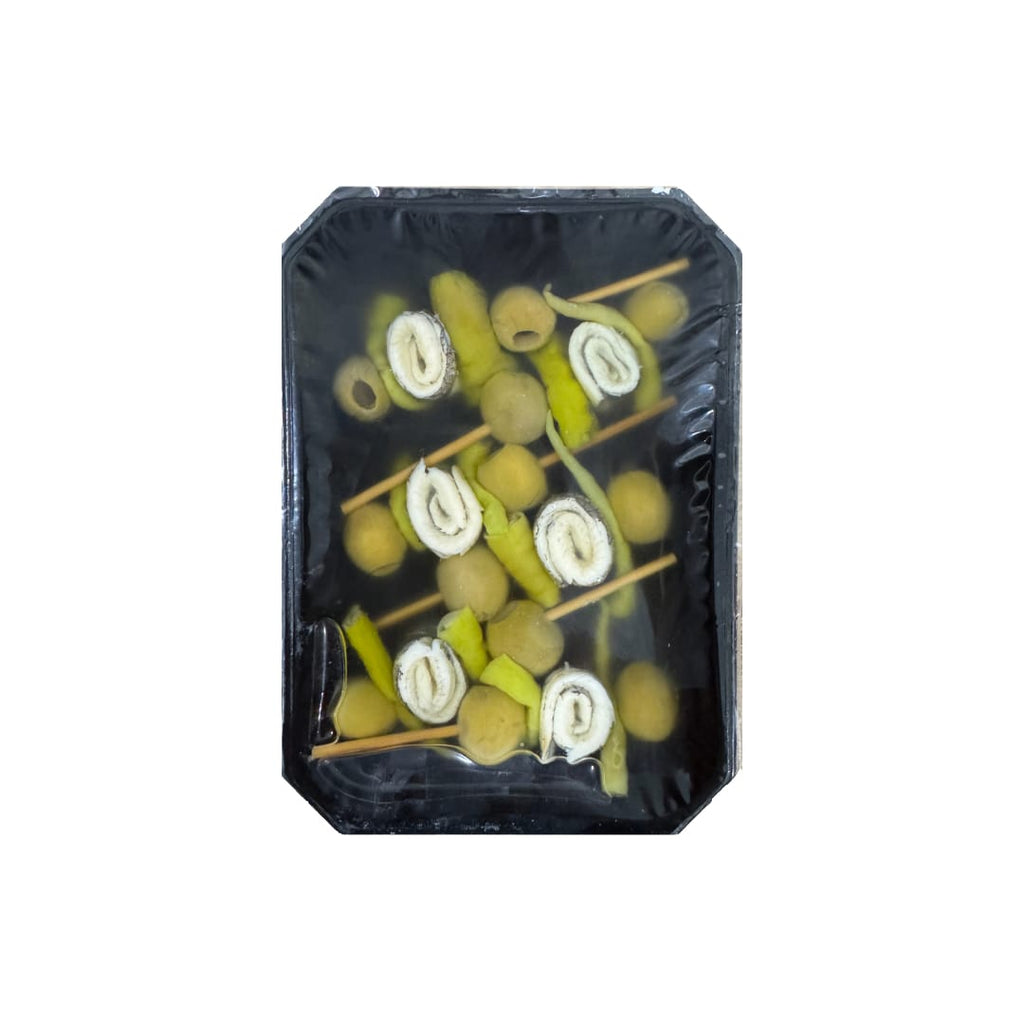 Packaged skewers of boquerones anchovies, olives, and pickled green peppers on a black background.