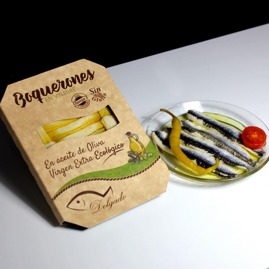 Packaging and a glass dish displaying boquerones (Spanish white anchovies) marinated in vinegar and preserved in organic extra virgin olive oil.