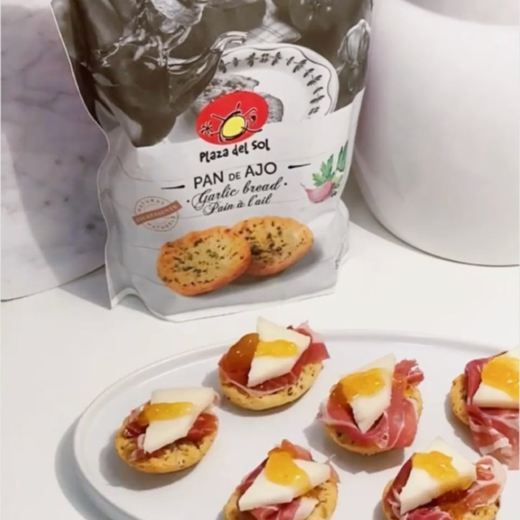 Packaging of Plaza del Sol Garlic & Parsley Bread Toasts with several toasts displayed in front, topped with meat and cheese.