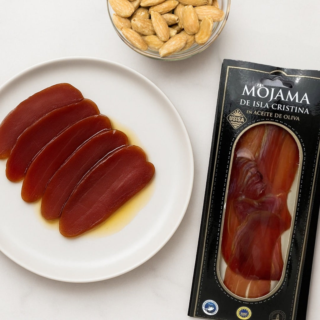 Sliced mojama on a plate with a packaging box and almonds in the background.