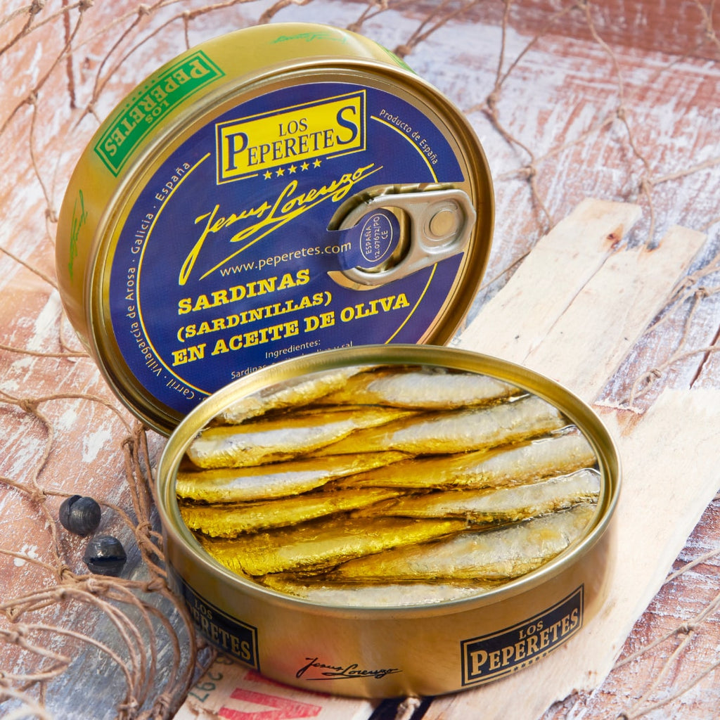 A tin can of Los Peperetes small sardines in olive oil, with the sardines visible inside the open can, placed on a wooden surface.